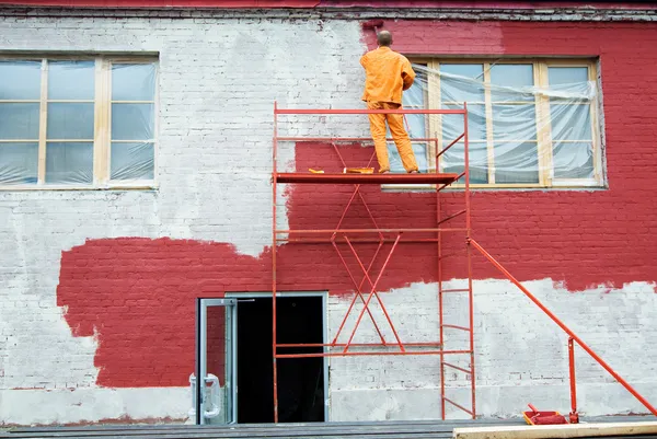 Building in progress with a professional painter applying a fresh red finish illustrating an exterior painter in Central Point, OR.